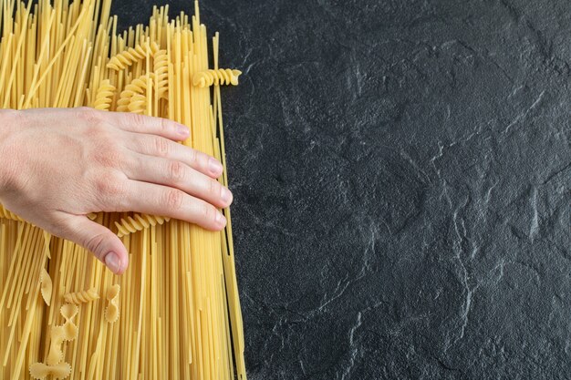 Mains féminines touchant diverses pâtes sur une surface sombre.