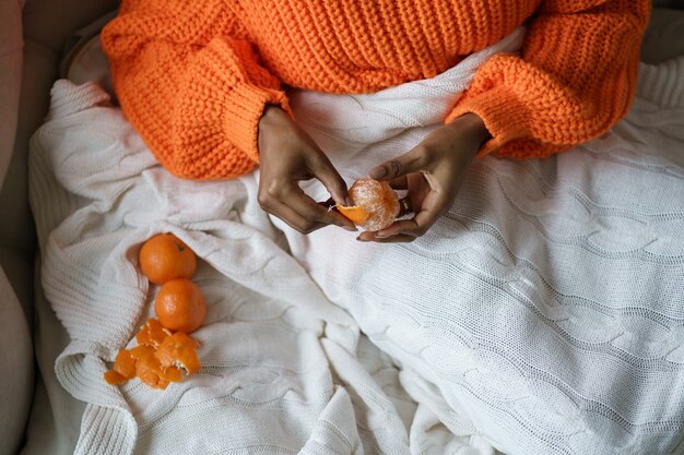 Mains De Femme Afro Peler La Mandarine Douce Mûre, Porter Un Pull Orange,  Couché Dans Son Lit Sous Le Plaid | Photo Premium