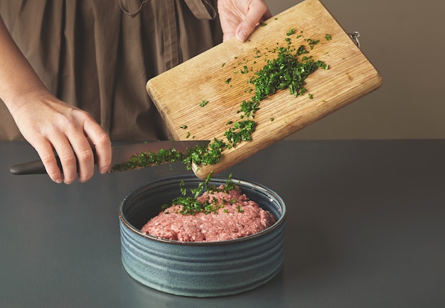 Photo gratuite mains de femme ajouter du persil vert frais à la viande hachée dans un beau bol en céramique sur la vieille table en bois