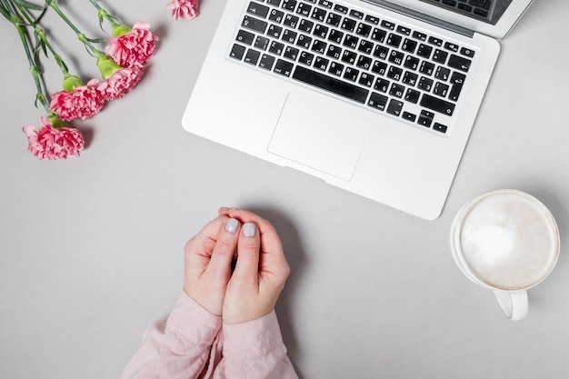 Mains de femme avec café et ordinateur portable fleurs oeillets sur fond blanc espace de travail de printemps arrière-plan vue de dessus