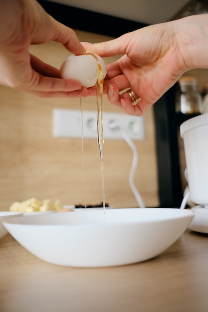 Mains de femme casse des œufs de poule dans un bol dans la cuisine.