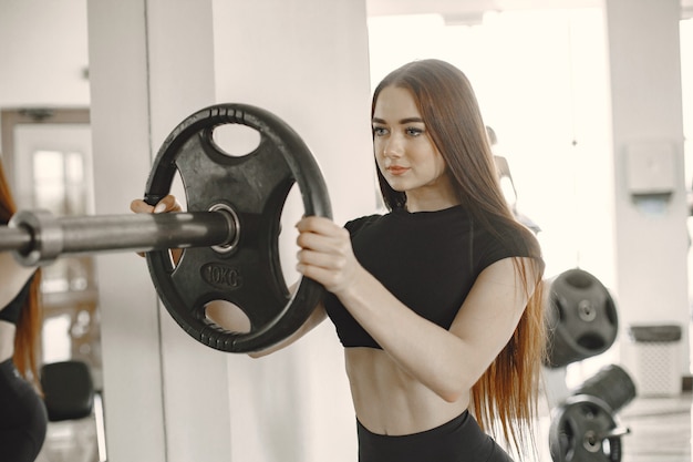 Les mains d'une femme forte tenant le disque de la barre et le mettant sur les disques de fer dans la salle de sport. une jeune femme musclée tient un disque de fer d'haltères.