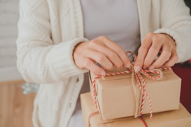 Mains d'une femme méconnaissable attachant des cadeaux de Noël avec une ficelle décorative