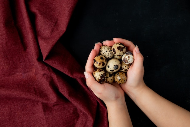 mains de femme pleine de mini oeufs sur table bordeaux et noir