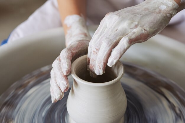 Mains de femme potier non reconnaissable confectionnant un vase en argile sur une roue de lancement