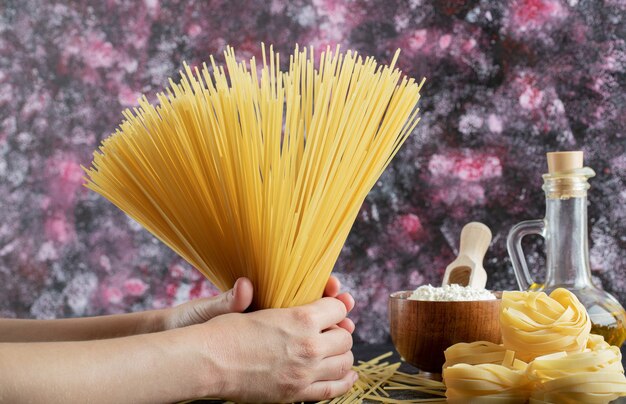 Mains de femme tenant des spaghettis sur fond coloré avec de l'huile et de la farine. photo de haute qualité