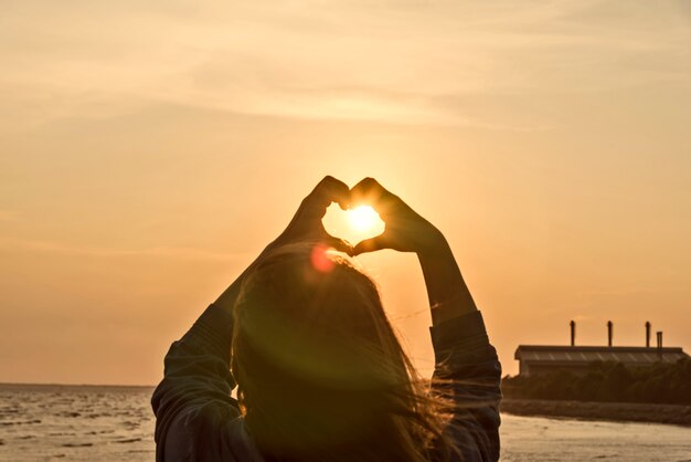 Les mains formant une forme de coeur avec la silhouette du coucher du soleil