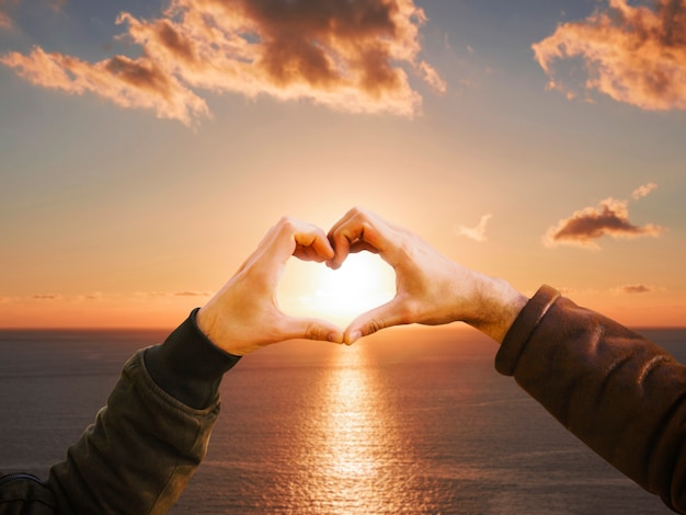 Photo gratuite mains en forme de coeur sur un coucher de soleil