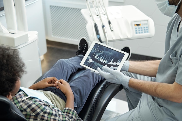 Mains gantées de stomatologue avec tablette affichant radiographie de dents humaines
