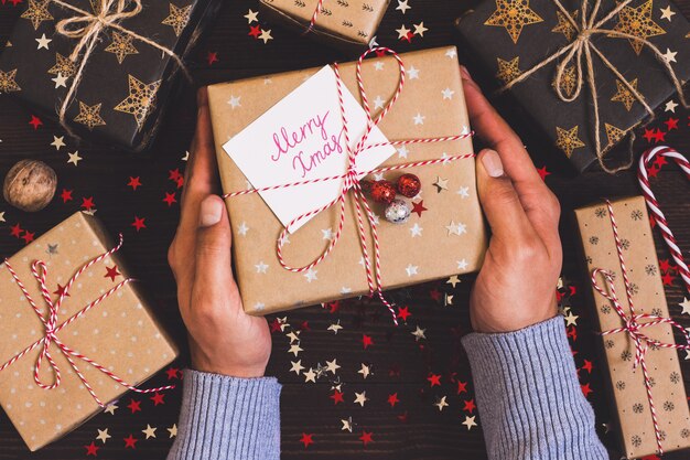 Mains d&#39;homme tenant une boîte de cadeau de vacances de Noël avec carte postale joyeux Noël sur la table de fête décorée
