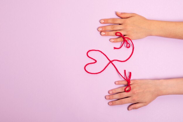 Mains humaines connectées avec un fil rouge en forme de coeur