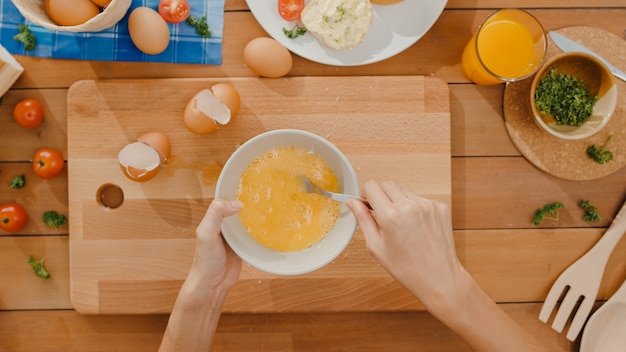 Mains de jeune chef de femme asiatique oeuf de craquage dans un bol en céramique et omelette de cuisson