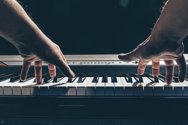 Les mains masculines jouent les touches du piano dans l'obscurité