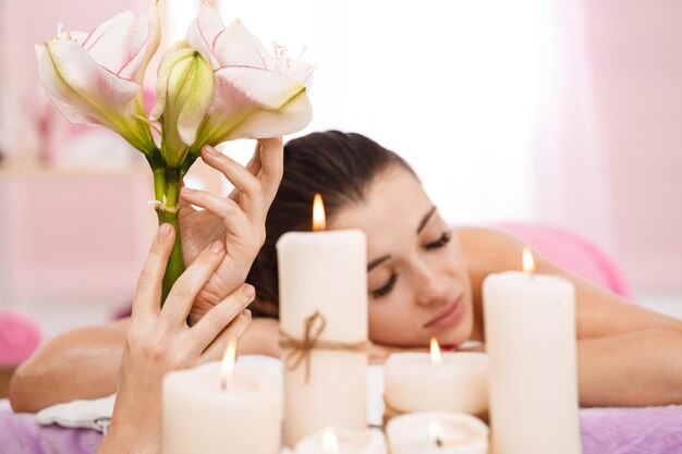 Mains de masseur tenant de belles fleurs derrière des bougies Détente et confort