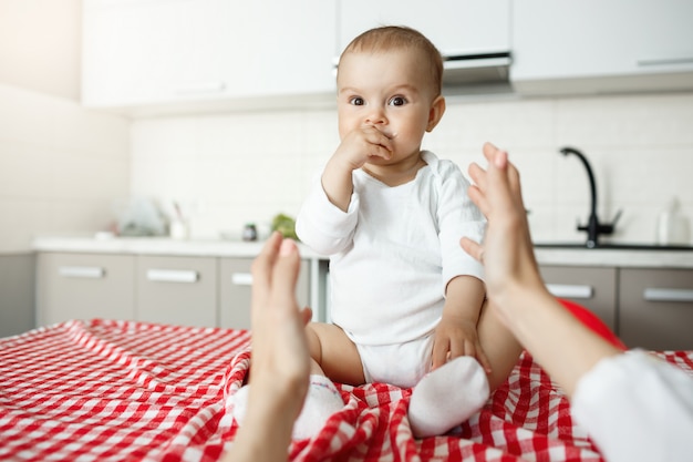 Mains de la mère atteignant son joli bébé assis sur un bureau