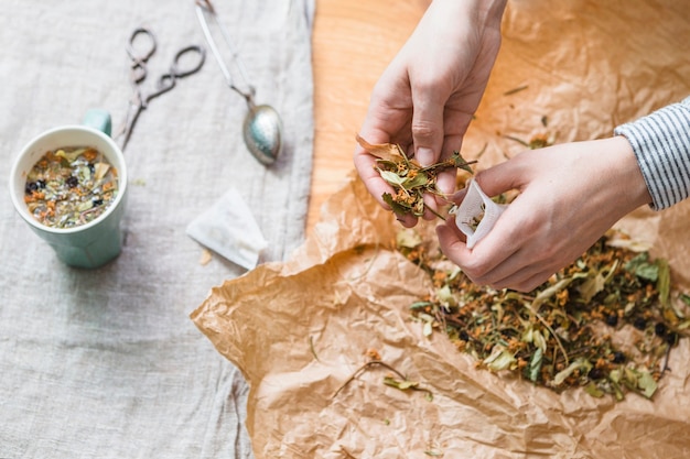 Mains mettant le mélange à base de plantes dans le sachet de thé