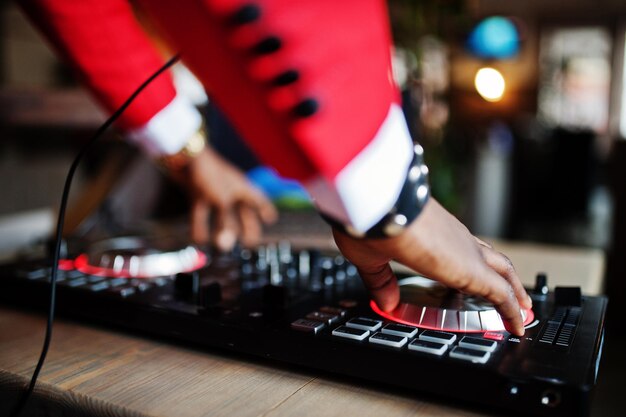 Mains de mode homme afro-américain modèle DJ en costume rouge avec contrôleur dj