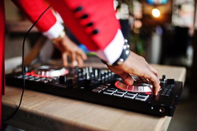 Mains de mode homme afro-américain modèle DJ en costume rouge avec contrôleur dj