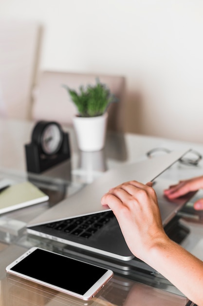 Mains ouvrant un ordinateur portable près de smartphone sur la table