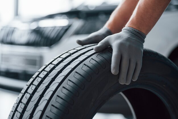 Mains seulement. Mécanicien tenant un pneu au garage de réparation. Remplacement des pneus d'hiver et d'été