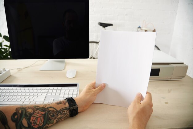 Des mains tatouées tiennent un paquet de feuilles de papier vierges avant de le charger dans le bac de l'imprimante domestique sur le bureau de travail