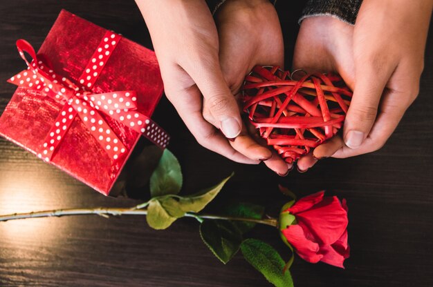 Mains tenant un coeur avec un cadeau et une rose