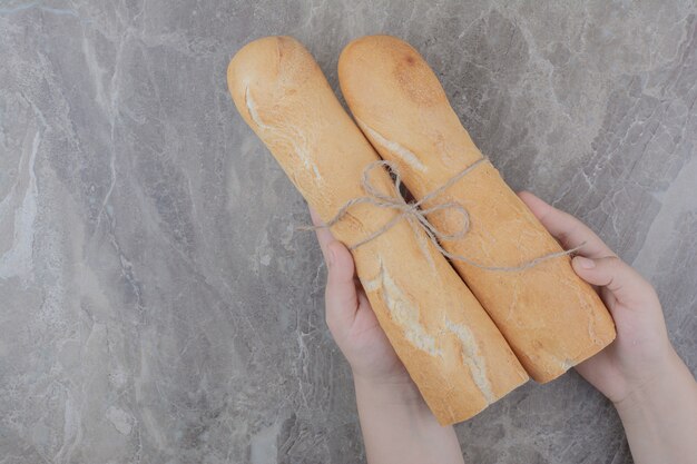 Mains tenant une demi-coupe de pain baguette français sur une surface en marbre