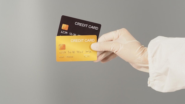 Les mains tiennent deux cartes de crédit noires et dorées sur fond gris la main porte une combinaison epi et un gant médical blanc