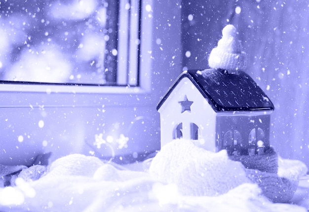 La maison confortable est enveloppée dans un chapeau et une écharpe dans un décor de rebord de fenêtre de tempête de neige. hiver, neige - isolation de la maison, protection contre le froid et les intempéries, système de chauffage des pièces. ambiance festive, noël, nouvel an