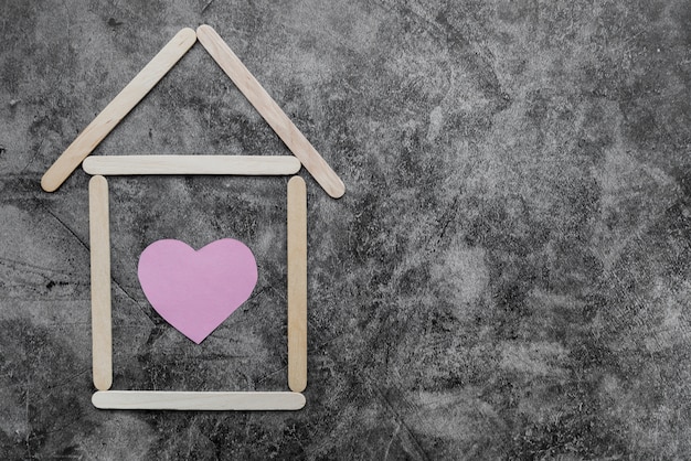 Maison faite de bâtons de glace en bois avec forme de coeur sur le mur noir grunge