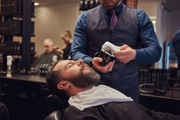 Un maître coiffeur prépare le visage au rasage, distribue de la mousse.