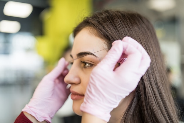 Maître faisant doucement la procédure des sourcils pour un joli modèle féminin