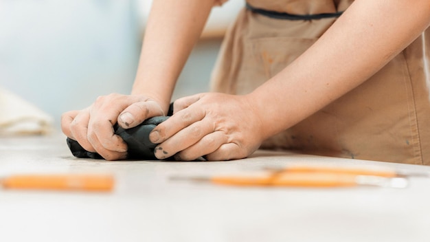 Photo gratuite le maître de la poterie sculptante travaillant dans un studio pétrir un morceau d'argile avec ses mains outils