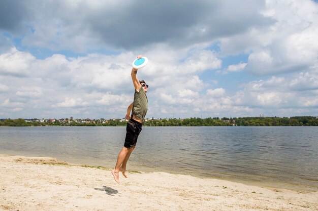 Mâle actif jouant au frisbee sur la plage de sable fin