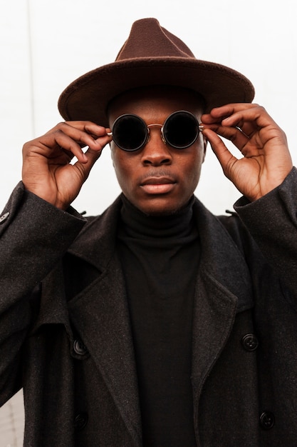 Mâle adulte élégant posant avec des lunettes de soleil et un chapeau