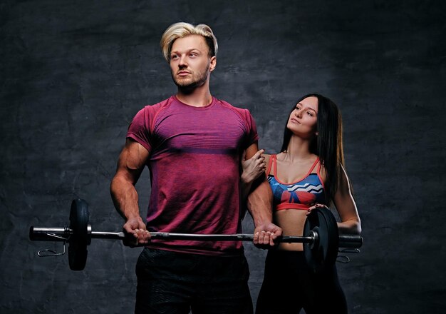 Le mâle athlétique et blond détient un poids d'haltère et un modèle féminin de fitness mince sur fond gris foncé.