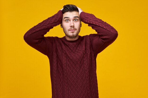 Mâle aux yeux de bogue surpris en pull chaud tenant les mains sur sa tête,