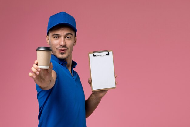 Mâle courrier en uniforme bleu tenant une tasse de café marron avec bloc-notes sur rose, prestation de services uniforme des travailleurs