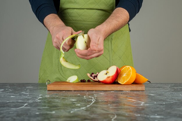 Mâle main éplucher la pomme verte sur le dessus de la planche de bois sur la table.