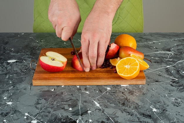 Mâle main tranche pomme rouge sur le dessus de la planche de bois sur la table.