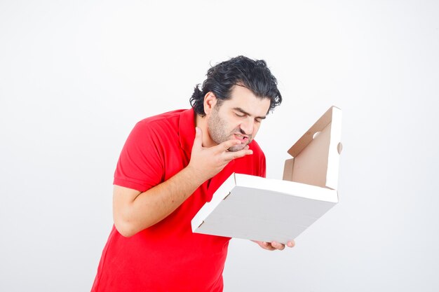 Mâle mature en t-shirt rouge à la recherche de boîte à pizza ouverte et à la faim, vue de face.