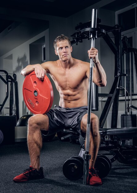 Le mâle musclé torse nu tient le poids de la barre dans un club de gym.