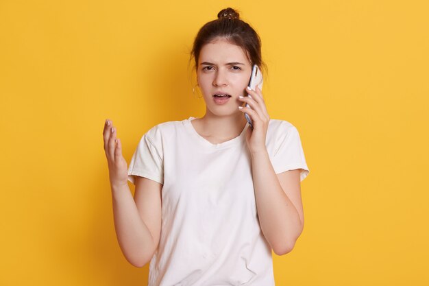 Malentendu jeune femme en vêtements décontractés posant contre le mur jaune