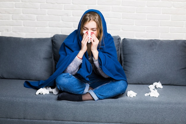 Malheureuse femme fatiguée bouleversée est assise sur un canapé à la maison souffrant d'un rhume et à l'aide de serviettes, avoir froid