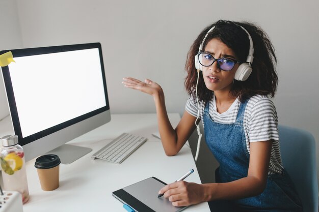 Malheureuse femme noire en denim pointant sur l'écran de l'ordinateur se plaint de la mauvaise connexion Internet