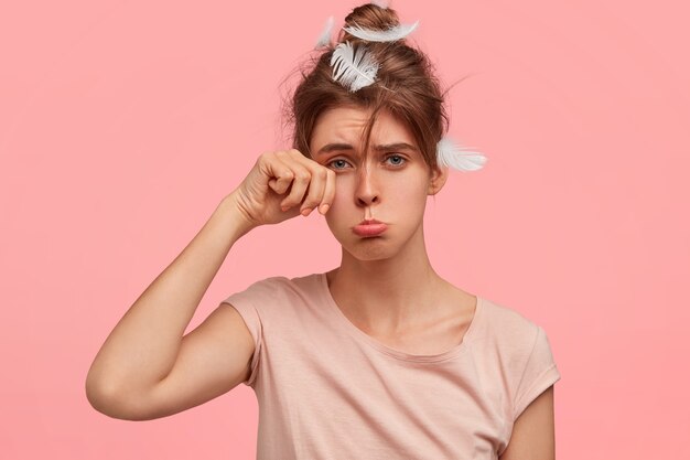 Malheureuse femme triste frotte les yeux et porte la lèvre inférieure, a une expression somnolente, insatisfaite car elle n'a pas assez dormi cette nuit