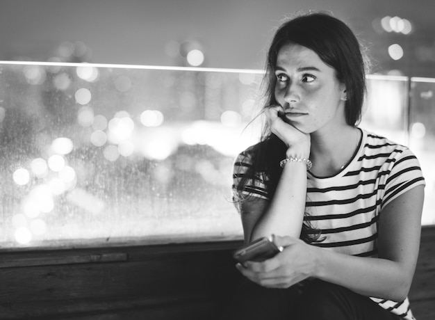 Malheureuse jeune femme tenant un smartphone dans le paysage urbain du soir