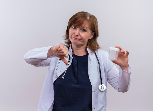 Malheureux femme médecin d'âge moyen portant robe médicale et stéthoscope tenant bécher médical et montrant le pouce vers le bas sur fond blanc isolé