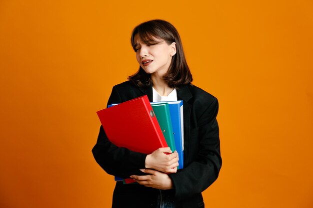 Malheureux tenant des dossiers jeune belle femme portant une veste noire isolée sur fond orange