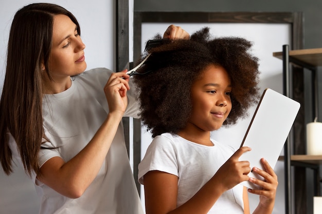 Photo gratuite maman aidant son enfant à coiffer les cheveux afro